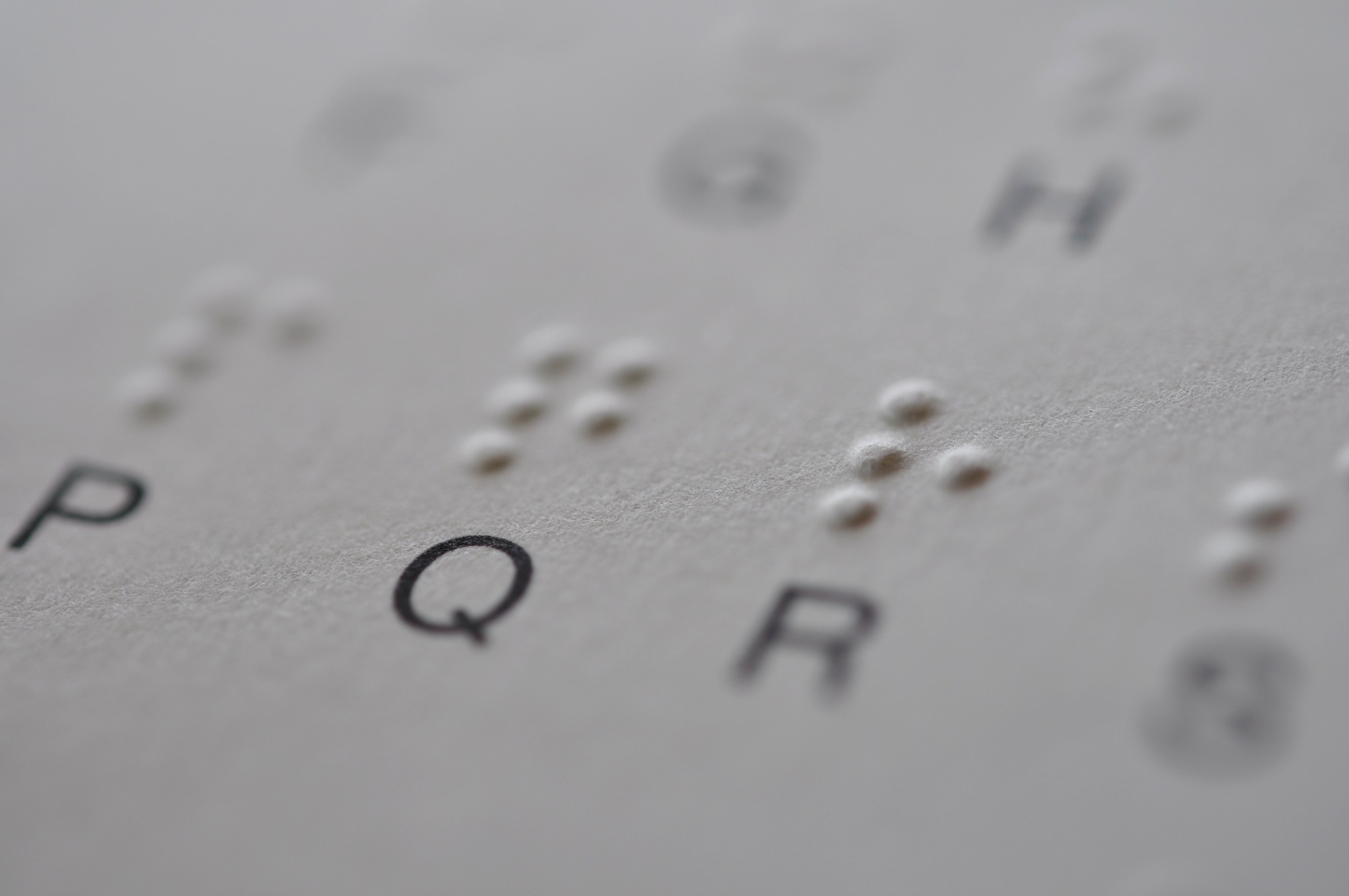 Close-up photograph of raised braille dots embossed on paper beside printed letters.