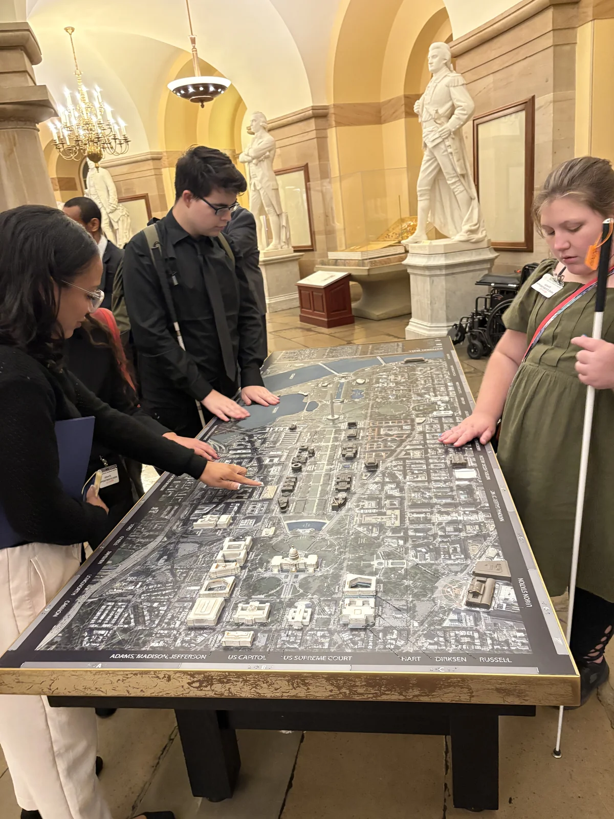 Isabelle and two other visitors explore a raised map in a marble hall.