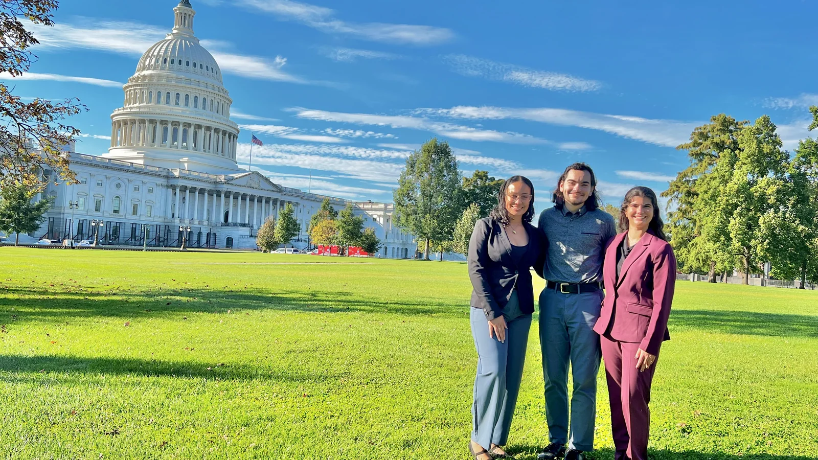 Three members of the group stand together with the Capitol behind them.