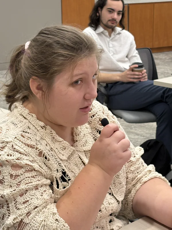 Isabelle holds a microphone while seated at a meeting table.