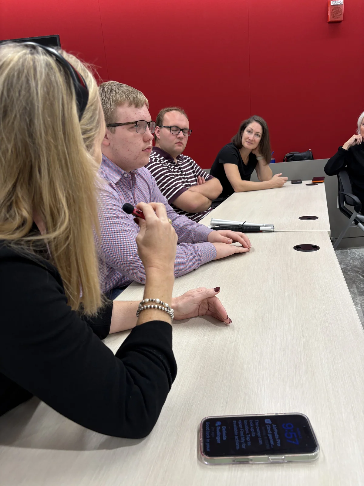 Participants sit around a conference table as a man holds a microphone.