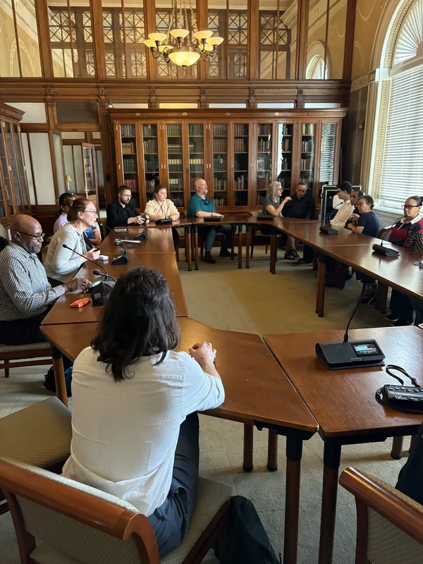 The group gathers around a long table in an ornate Library of Congress room.