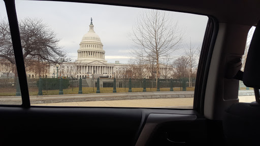 The dome and facade of the United States Capitol under an overcast sky, seen through a car window on arrival in Washington, D.C.