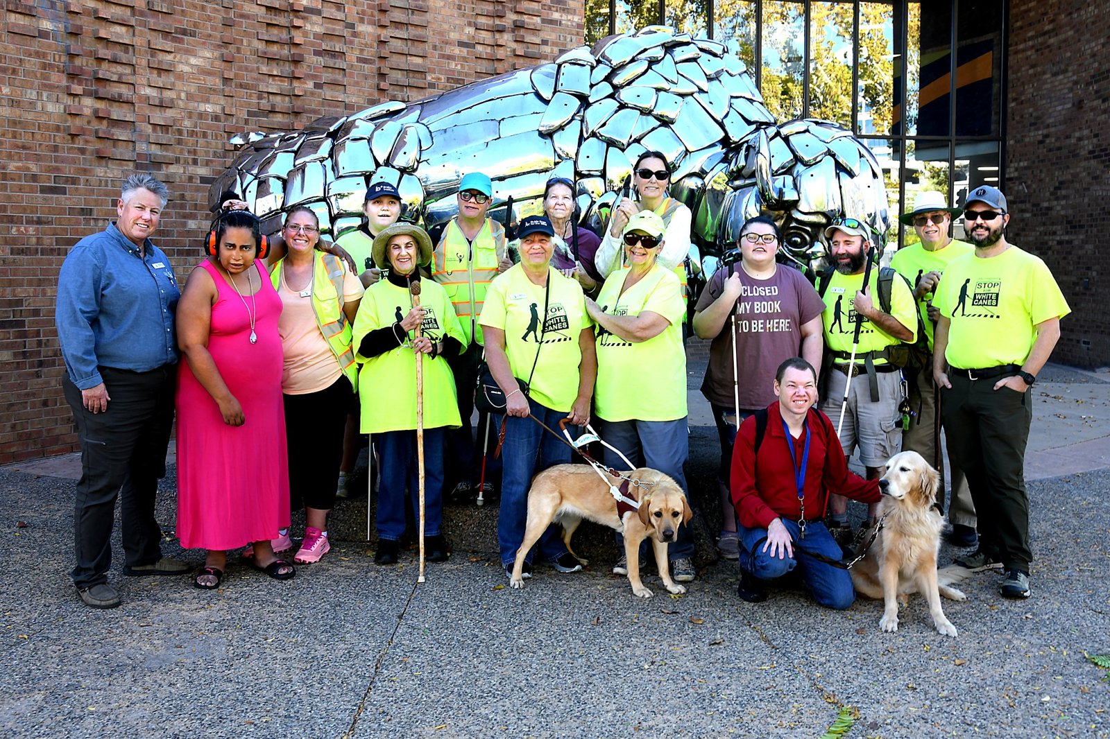 White Cane Day participants gather with white canes and guide dogs; several wear Stop for White Canes shirts.